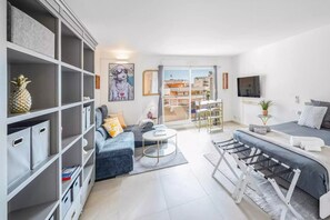 A modern living room with a sofa, coffee table, and TV. There is a bookshelf and a dining area with a table and chairs. - New large studio  sea view and lift and free parking (1.9m. max) upon request (Beausoleil)