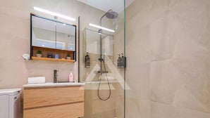 Een moderne badkamer met een glazen douchecabine, een houten wastafelmeubel en een spiegel boven de wastafel.