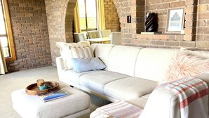 A cozy living room with a white sofa, a wooden coffee table, and a brick wall with arched windows. - Marvelous 4-bedroom house in Moonah (Moonah)