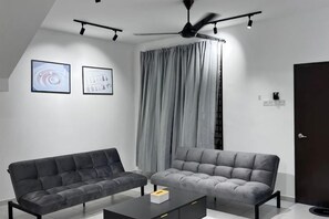 A modern living room with two sofas, a coffee table, and a ceiling fan. - Senai 14pax The Joyous Home Pooltable Airport JPO (Senai)