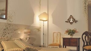A bedroom with a bed, bedside table, lamp, chair, and a mirror on the wall. - La Casa degli Archi (Cevoli)