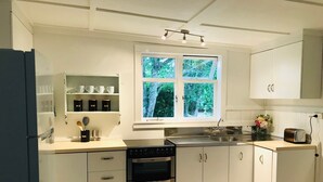Ett modernt kök med vita skåp, en inbyggd ugn, en dubbeldiskho och ett fönster med utsikt över grönområden.