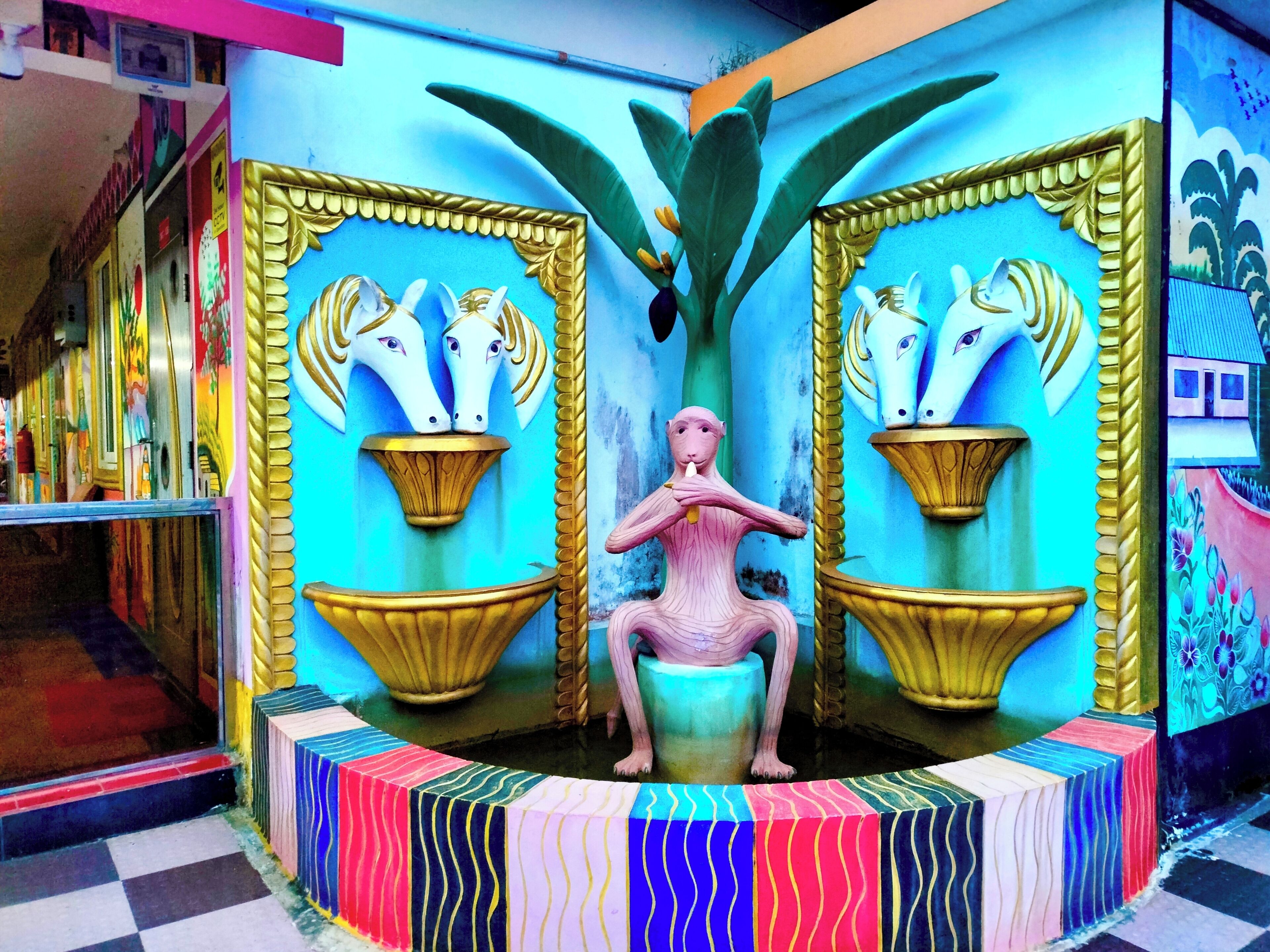 A colorful mural with a central figure and two horse heads in golden frames.