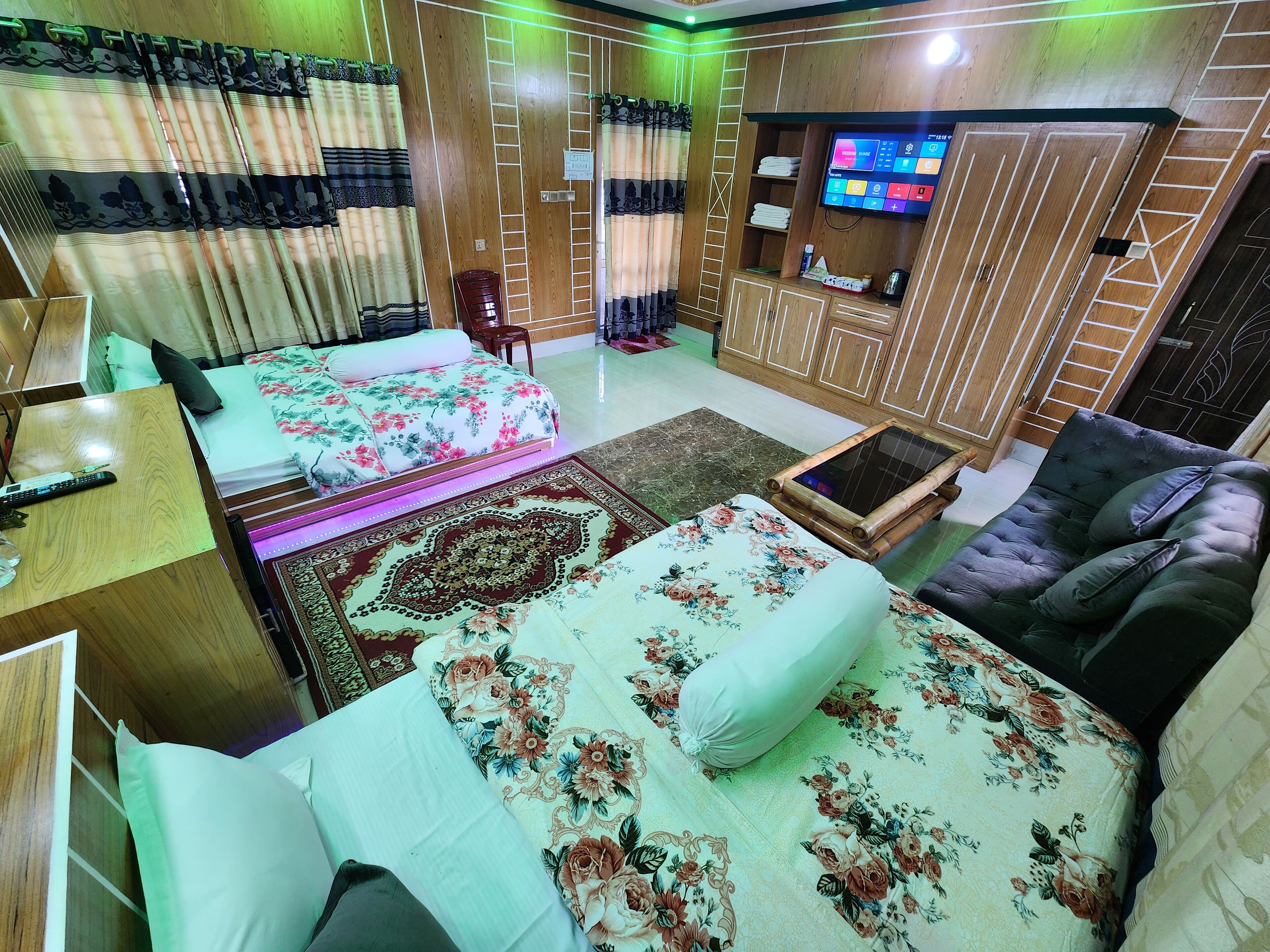 Una camera d'albergo con due letti, un divano, una televisione e un armadio in legno.