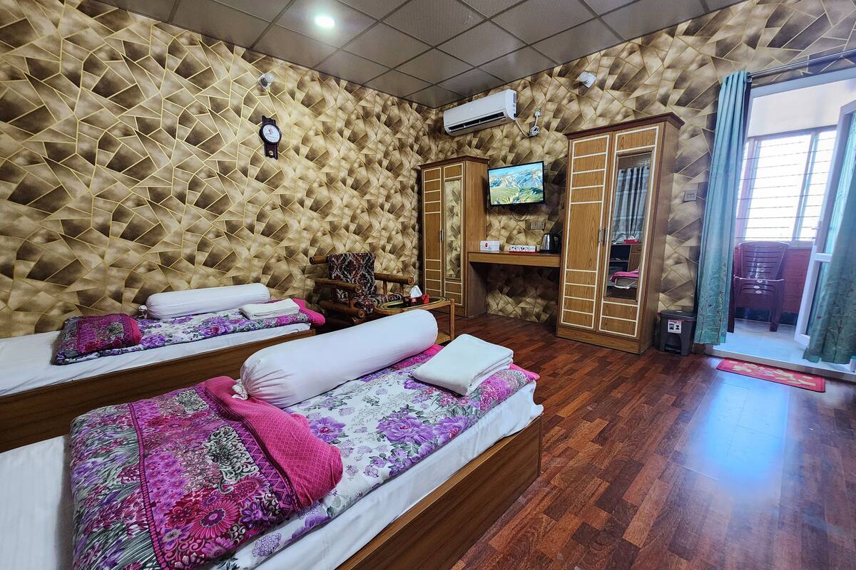 A hotel room with two beds, a television, a wardrobe, and a wooden floor.