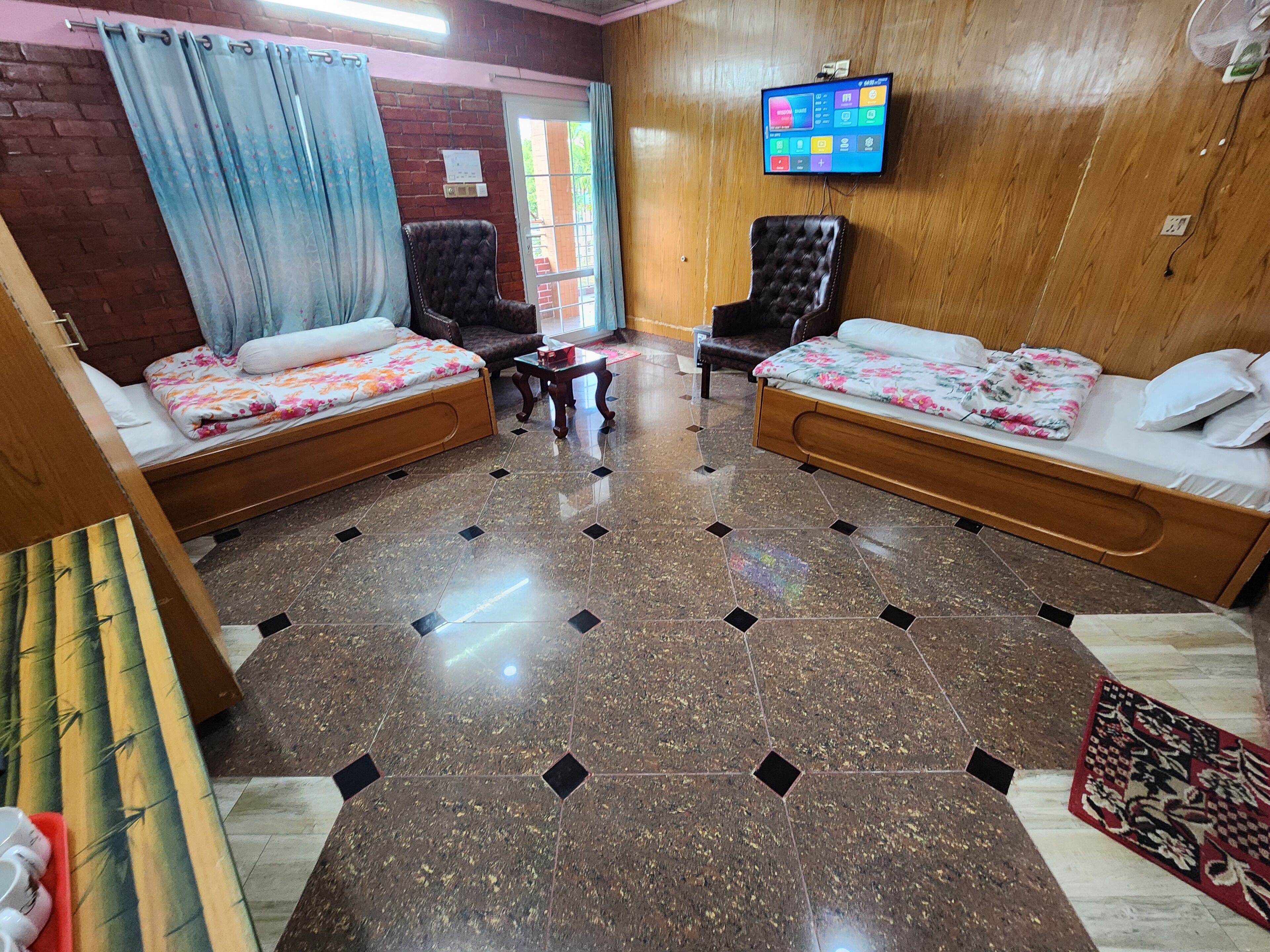 Habitación de hotel con dos camas de madera, una mesita, un televisor en la pared y un ventanal con cortinas.