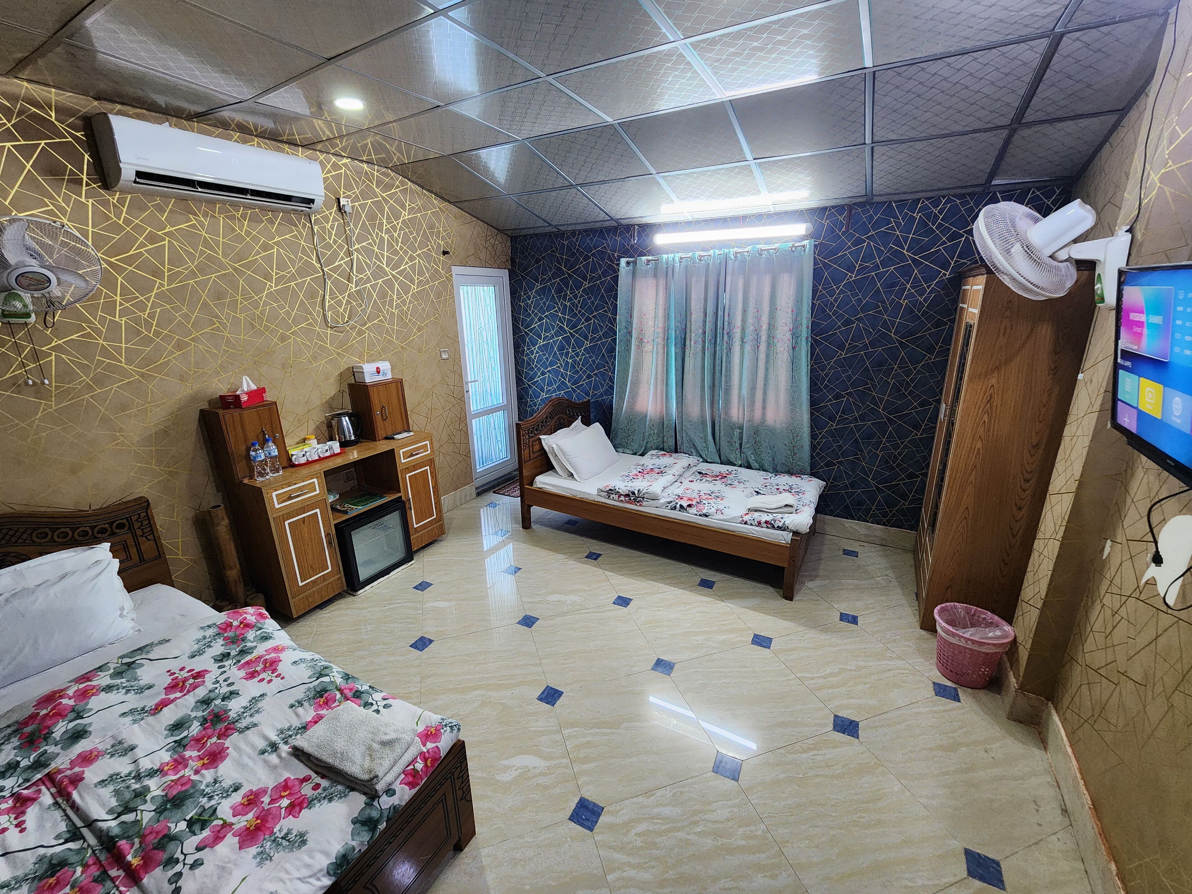 Une chambre d’hôtel équipée d’un lit, d’un bureau avec un ordinateur, d’un climatiseur, d’un ventilateur et d’une télévision.
