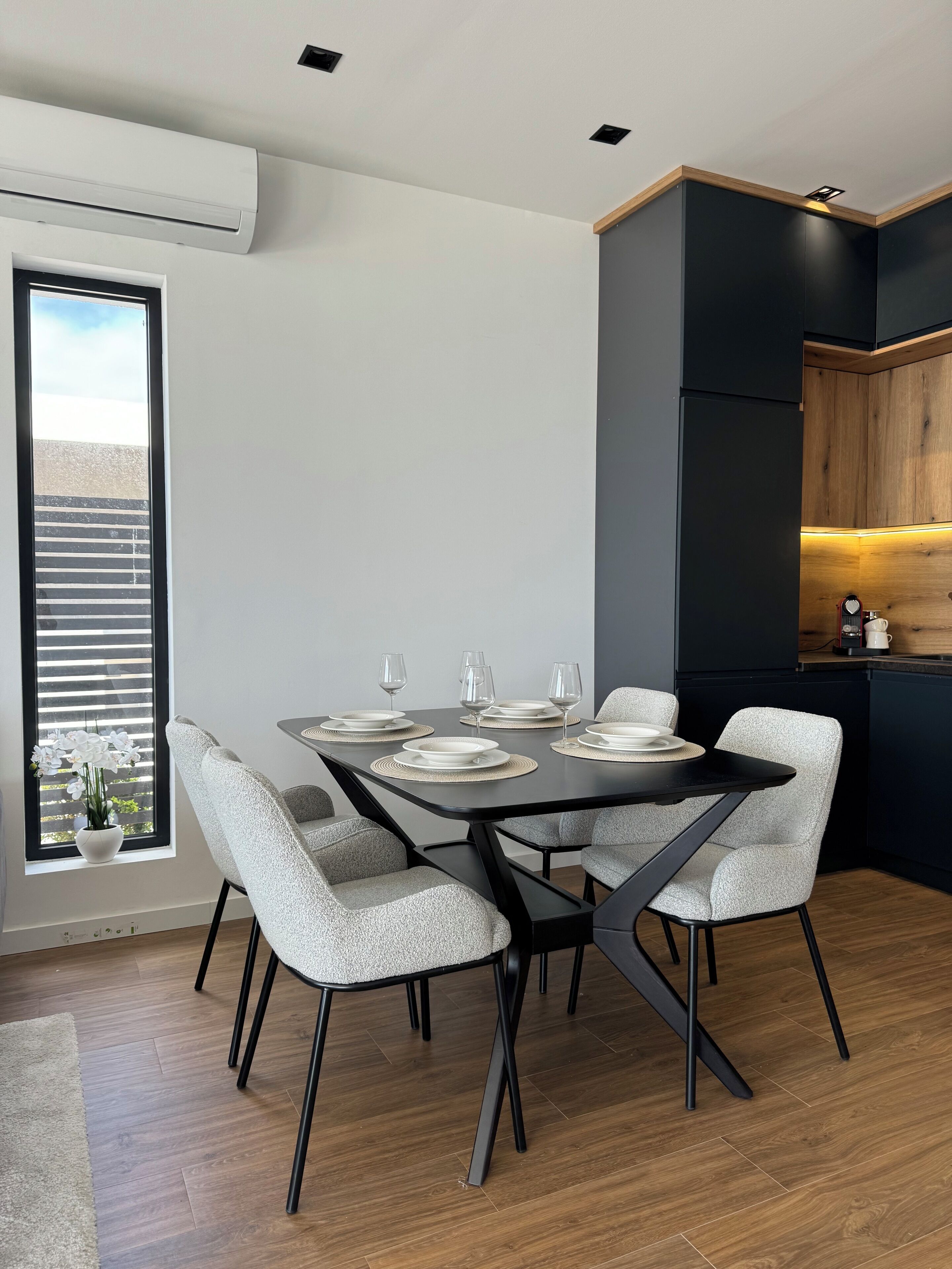 A modern dining area with a black table set for four, surrounded by grey upholstered chairs.