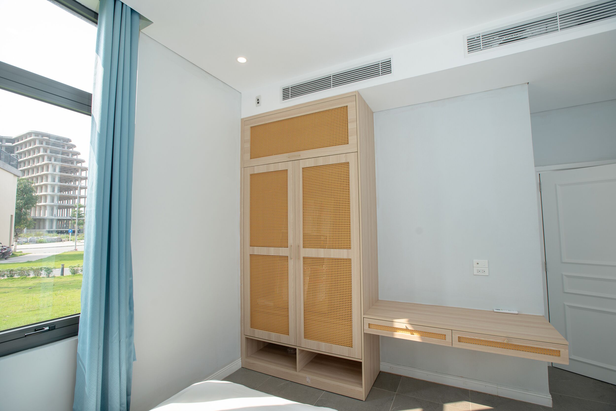 A modern room with a built-in wardrobe, a small desk, and a window with a view of buildings and greenery.