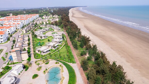 Luchtbeeld van een kustresort met meerdere gebouwen, een strand en een aangelegd zwembad.
