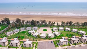 Een kustwoongebied met een cirkelvormige binnenplaats, omringd door moderne gebouwen, een strand en boten in de verte.