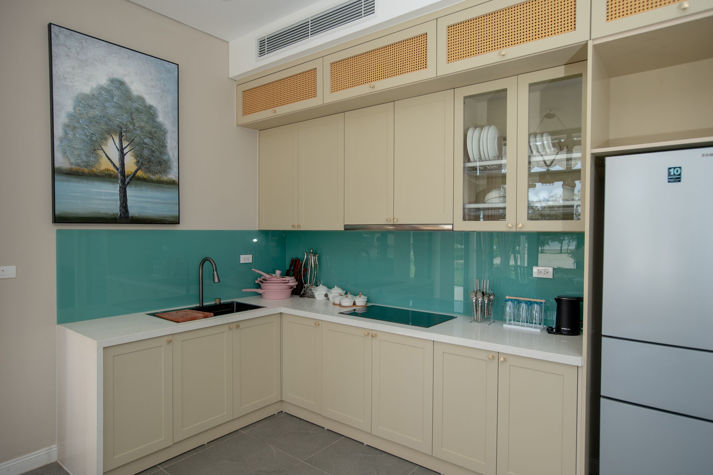 Una cocina con un lavamanos, armarios, un refrigerador y un cuadro en la pared.