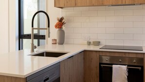 A modern kitchen with a white countertop, stainless steel sink, wooden cabinets, and a built-in oven. - Spacious Central Townhouse – Perfect for All (Christchurch)