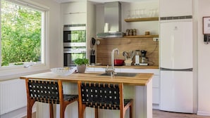 A modern kitchen with a wooden table, two chairs, a built-in oven, a coffee maker, and a refrigerator. - Leas Pärla by Interhome (Torup)