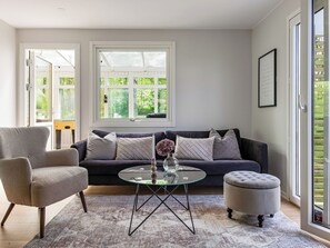 Moderni olohuone, jossa on sohva, nojatuoli, jalkarahi ja lasinen sohvapöytä.