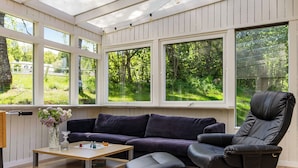 A conservatory with a dark-colored sofa, a wooden coffee table, and a black chair. - Leas Pärla by Interhome (Torup)