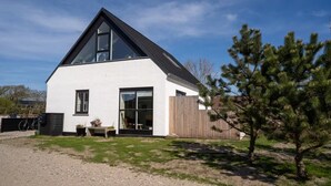 Ein modernes, zweistöckiges Haus mit geneigtem Dach, großen Fenstern und einem Holzzaun.