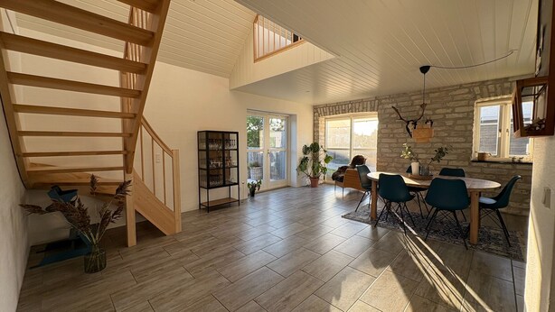 Ein geräumiges Wohnzimmer mit einer Holztreppe, einem Esstisch mit Stühlen und einem Bücherregal.