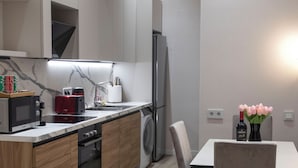 A modern kitchen with wooden cabinets, a built-in oven, a microwave, and a sink. There is a dining table with chairs and a vase of flowers. - MK Luxury Serviced Apartments #3 - Apt. 1 (Chișinău)