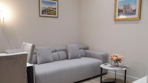 A modern living room with a grey sofa, a small round table with a vase of flowers, and two framed pictures on the wall. - MK Luxury Serviced Apartments #3 - Apt. 1 (Chișinău)