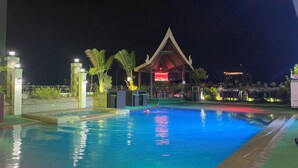 Un espace piscine nocturne avec un bar et un restaurant en arrière-plan.
