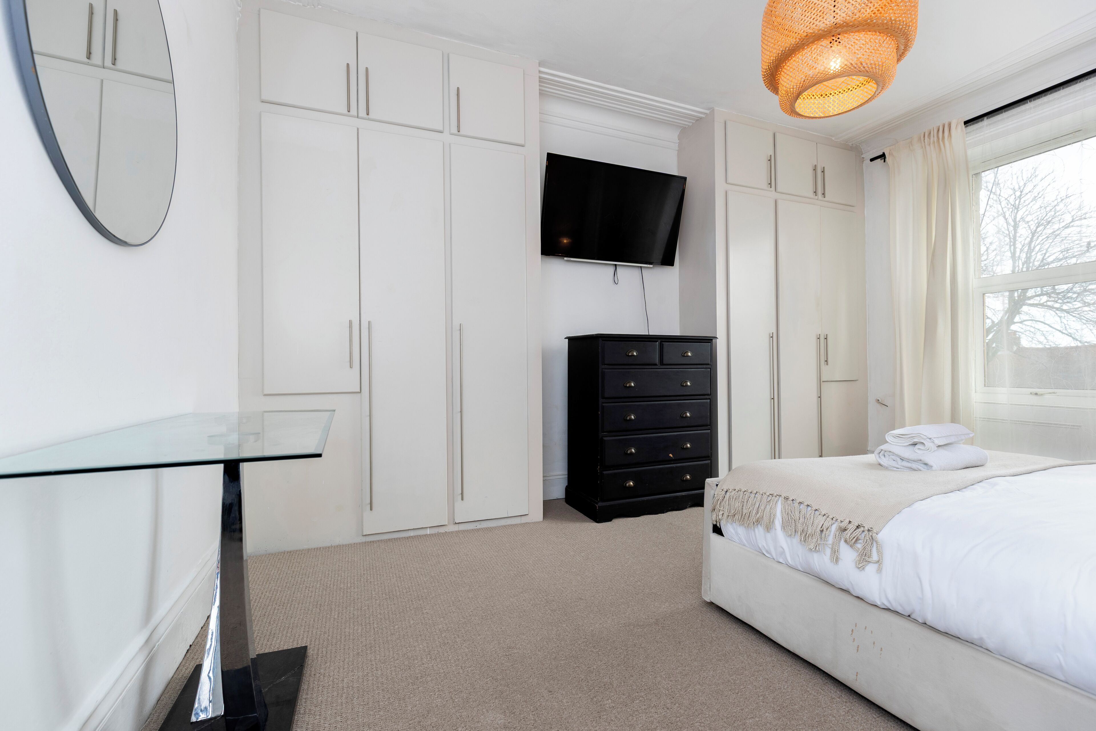 A bedroom with a bed, a dresser, a TV, and a glass table.