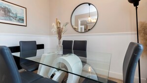 A modern dining area with a glass table, black chairs, a vase with dried flowers, a round mirror, and a framed picture on the wall. - Bright 4-bedroom Maisonette in Gateshead (Gateshead)