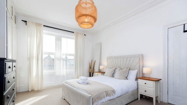 A bedroom with a bed, bedside tables, a dresser, and a window with curtains. - Bright 4-bedroom Maisonette in Gateshead (Gateshead)