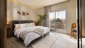 Un dormitorio moderno con una cama grande, un balcón con mesa y sillas, y vistas a la ciudad.