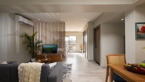Una sala moderna con televisor, sofá, mesa de centro y comedor con fruta.