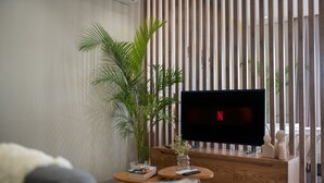 Una sala moderna con un televisor de pantalla plana mostrando el logotipo de Netflix, una planta grande en maceta y un mueble bajo para la televisión de madera.