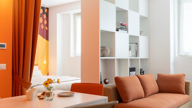 A modern living room with a sofa, a coffee table, and a bookshelf. - 7Studios - 4 orange (Milano)