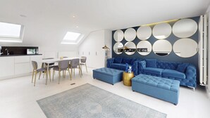Un salon moderne avec un canapé bleu, un coin repas avec une table et des chaises blanches, et un mur orné de miroirs ronds.