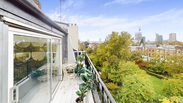 Un balcon avec une porte vitrée, des chaises en osier peintes en blanc et des plantes en pot.