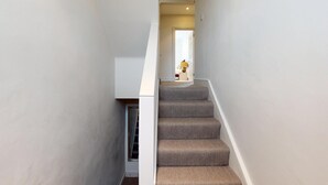 Un escalier étroit, avec des marches recouvertes de moquette, menant à un palier.