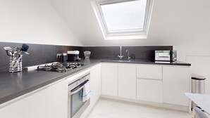 Une cuisine moderne dotée d’une verrière, de meubles blancs, d’une cuisinière en acier inoxydable et d’un plan de travail noir.