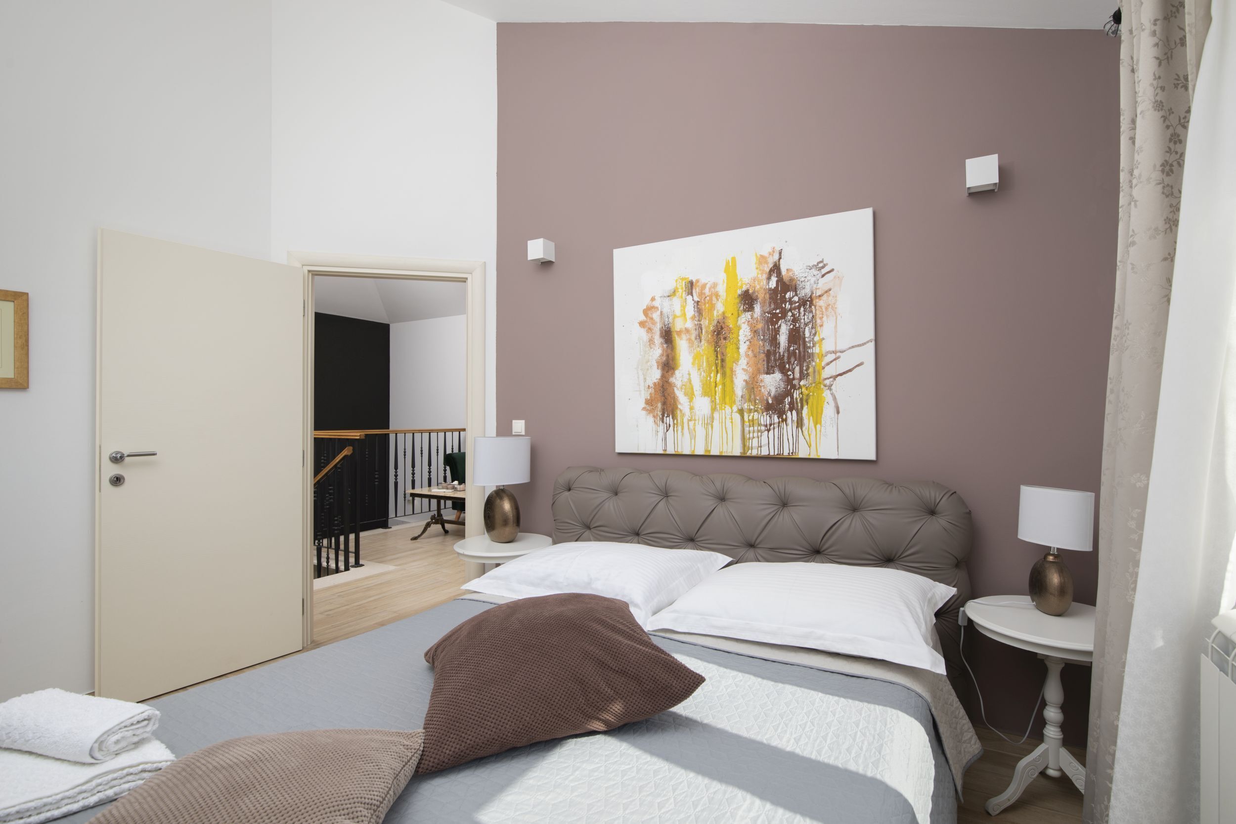 A bedroom with a bed, pillows, a nightstand, a lamp, and a painting on the wall.