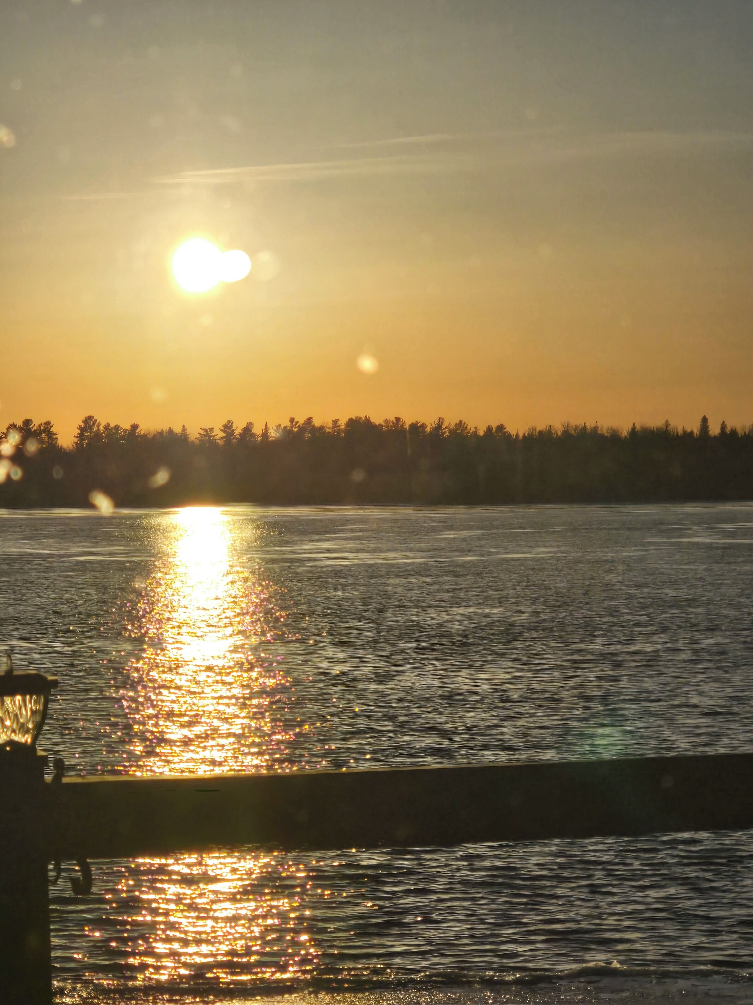 A sunset over a body of water with a silhouette of trees in the background.