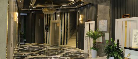 A modern lobby with a marble floor, a reception desk, and a staircase.