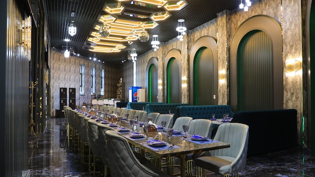 Una larga mesa de comedor con múltiples sillas, una zona de bar y una sección de estar con bancos acolchados.