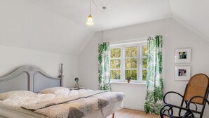 Une chambre à coucher avec un lit, un fauteuil à bascule, une fenêtre avec des rideaux et une petite table avec une lampe.