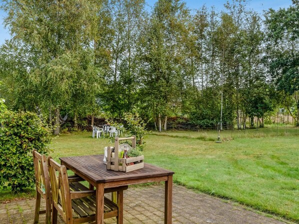 A wooden table with chairs and a small table lamp in a garden with a brick pathway.