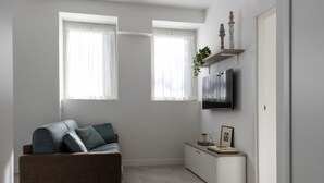 A modern living room with a sofa, a TV mounted on the wall, and a small cabinet. - 7Studios - 1 Sage (Milano)