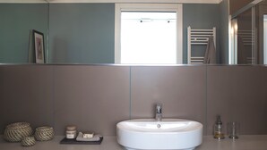 A bathroom with a large mirror, a white sink, and a window. - 7Studios - 1 Sage (Milano)
