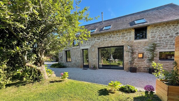 Ein Haus aus Stein mit einem Kiesweg, einem Baum und einem Blumenbeet.