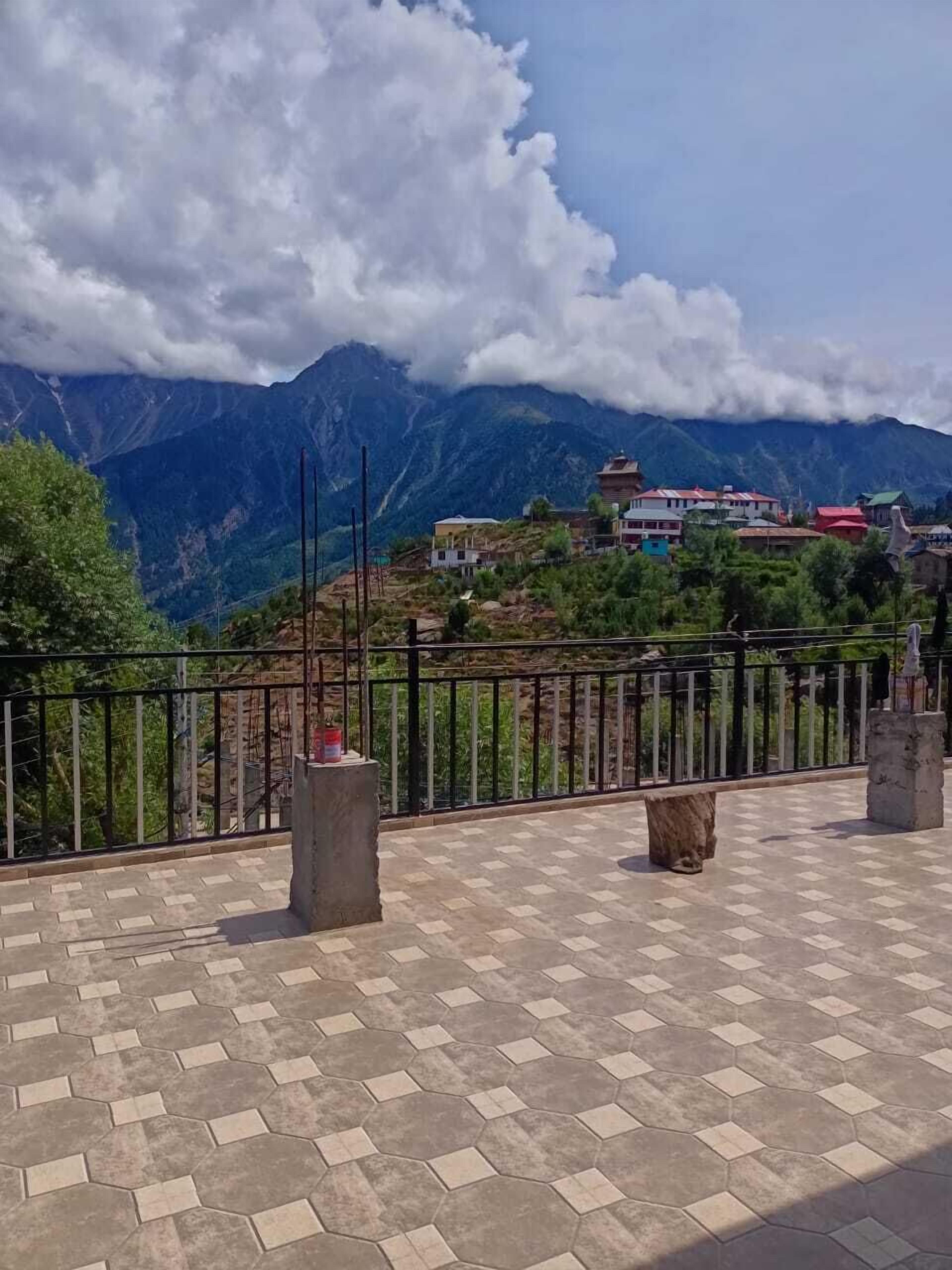 A terrace with a tiled floor, a metal railing, and a view of mountains and buildings in the background.