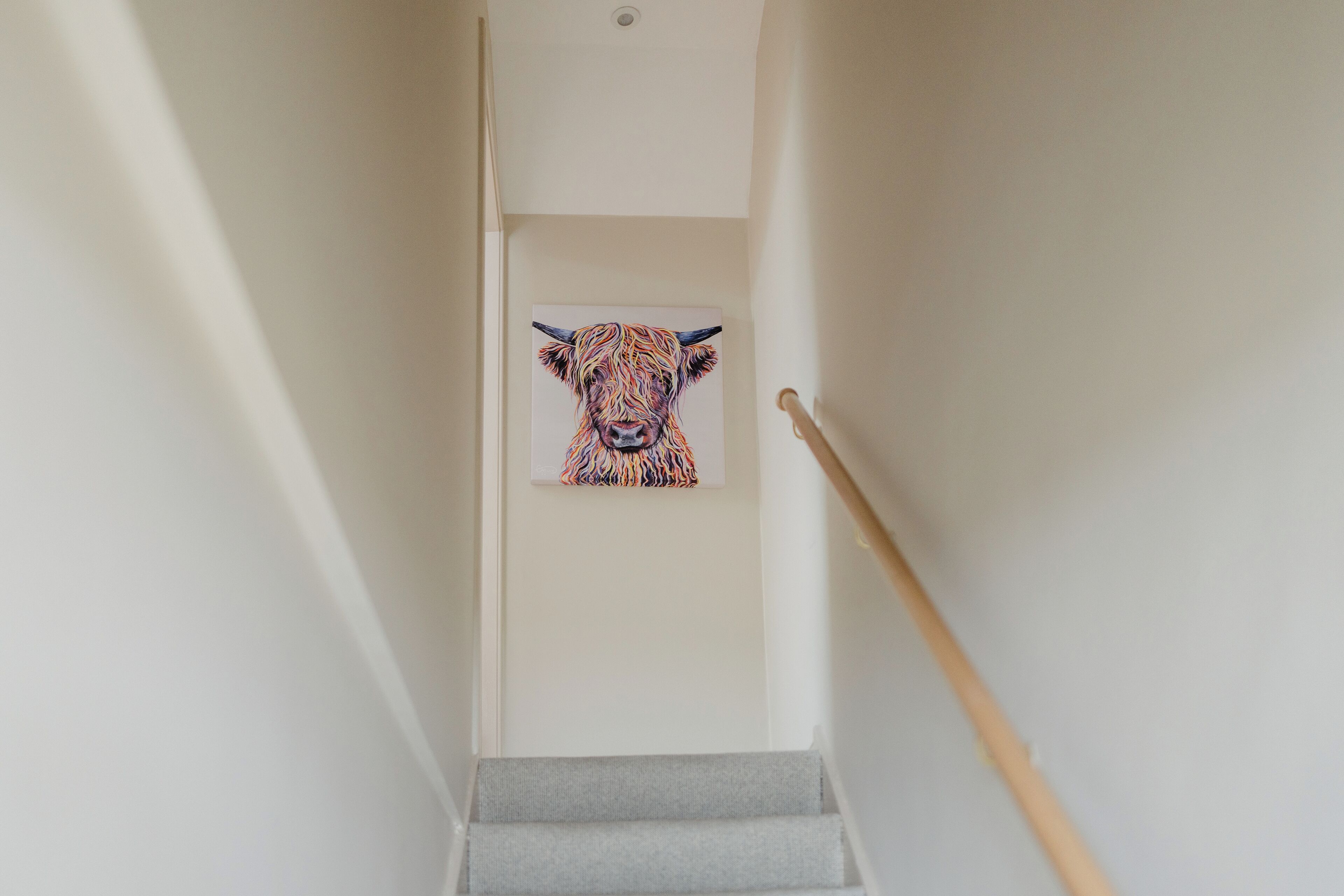 A staircase with a painting of a cow on the wall.