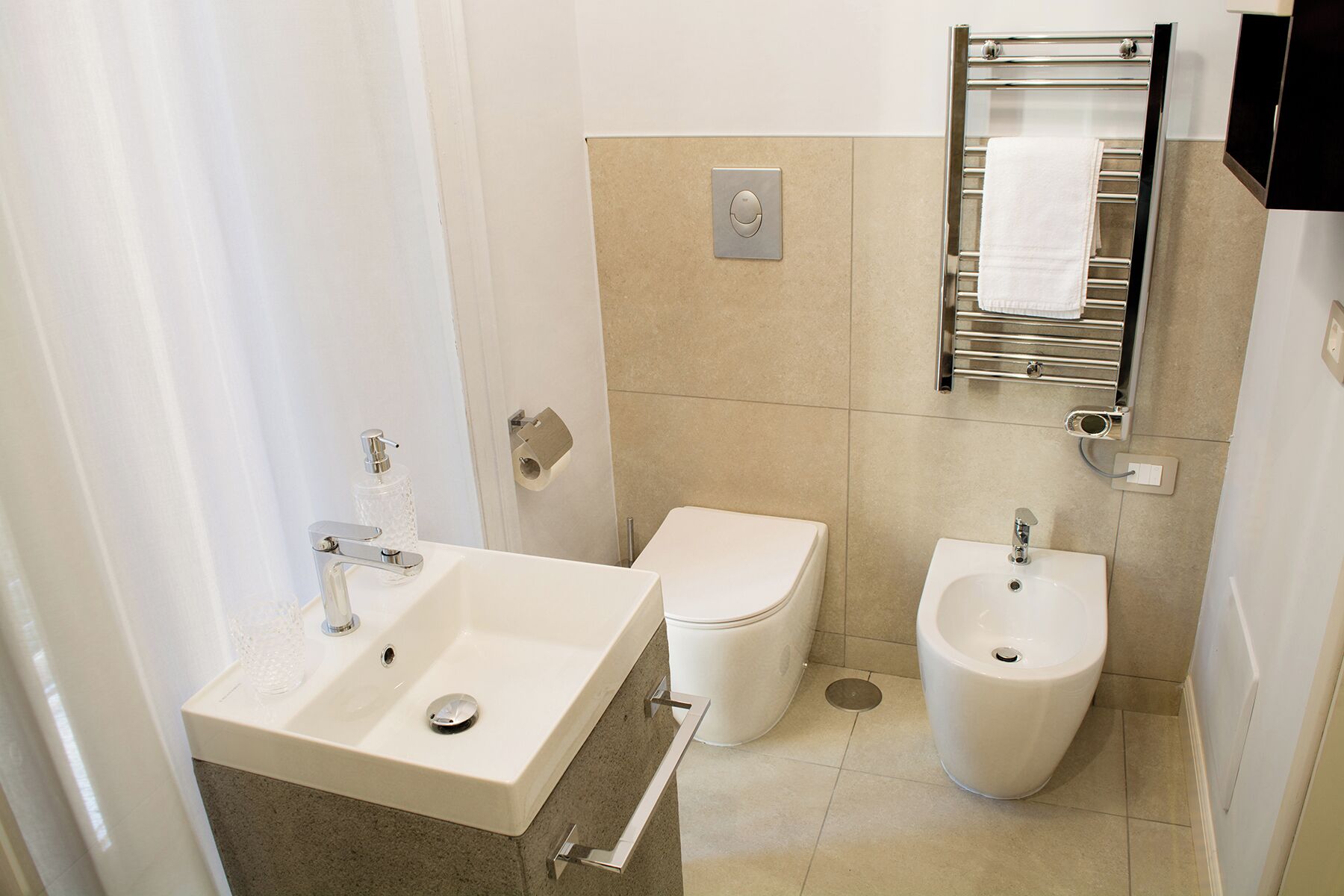 A modern bathroom with a sink, toilet, bidet, and towel rack.