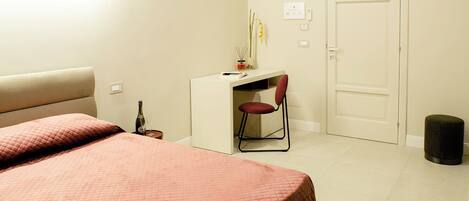 A bedroom with a bed, a desk, a chair, a door, and a trash bin.
