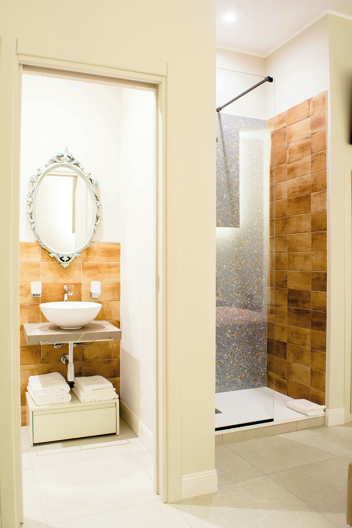A bathroom with a white sink, a mirror with an ornate frame, and a shower area with tiled walls.